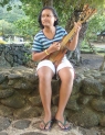 A vision from a painting by Paul Gauguin, this young girl plays her hand-carved guitar in front of a cemetery on the island Tahuata